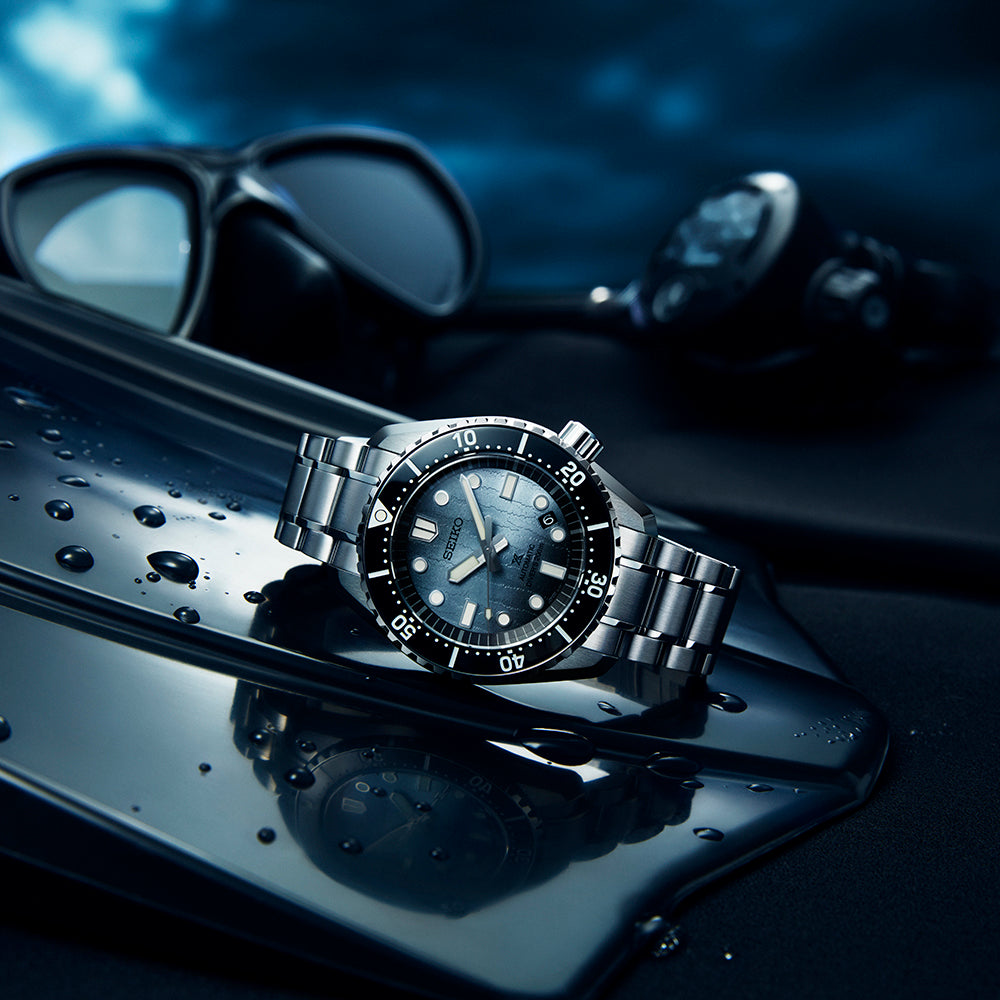 Silver watch with black face on a reflective surface