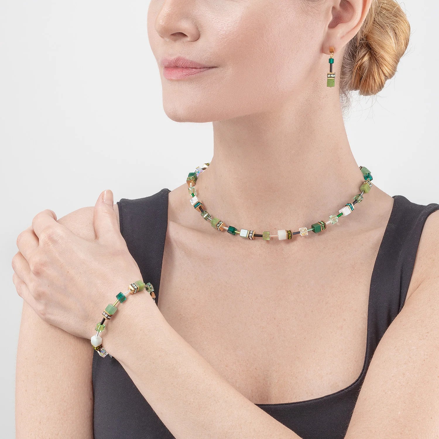 Woman wearing a green beaded necklace, bracelet, and earrings on a light gray background