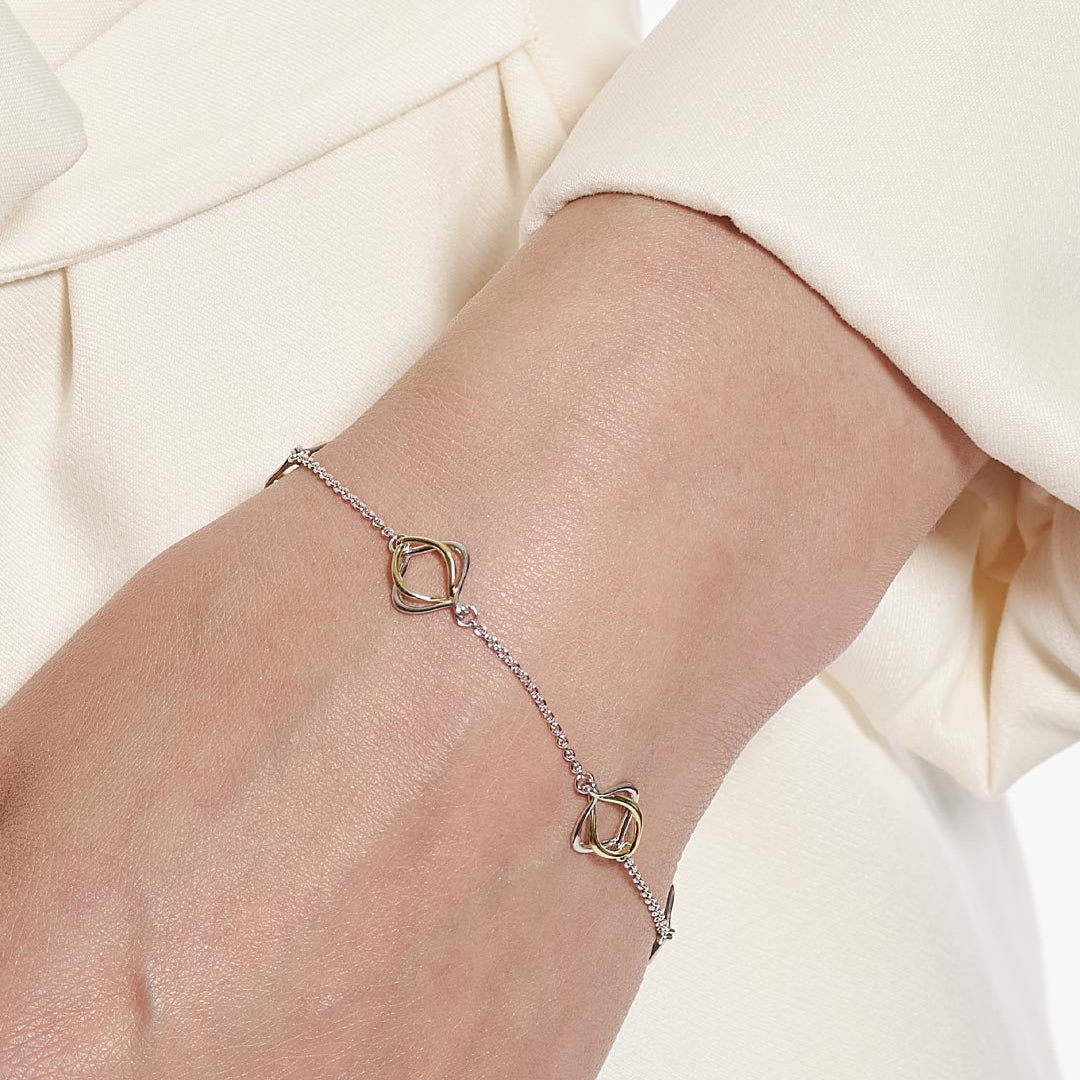 A delicate chain bracelet with two interlocking double-ring motifs in mixed gold and silver metals, shown worn on a person's wrist against a cream-colored top.