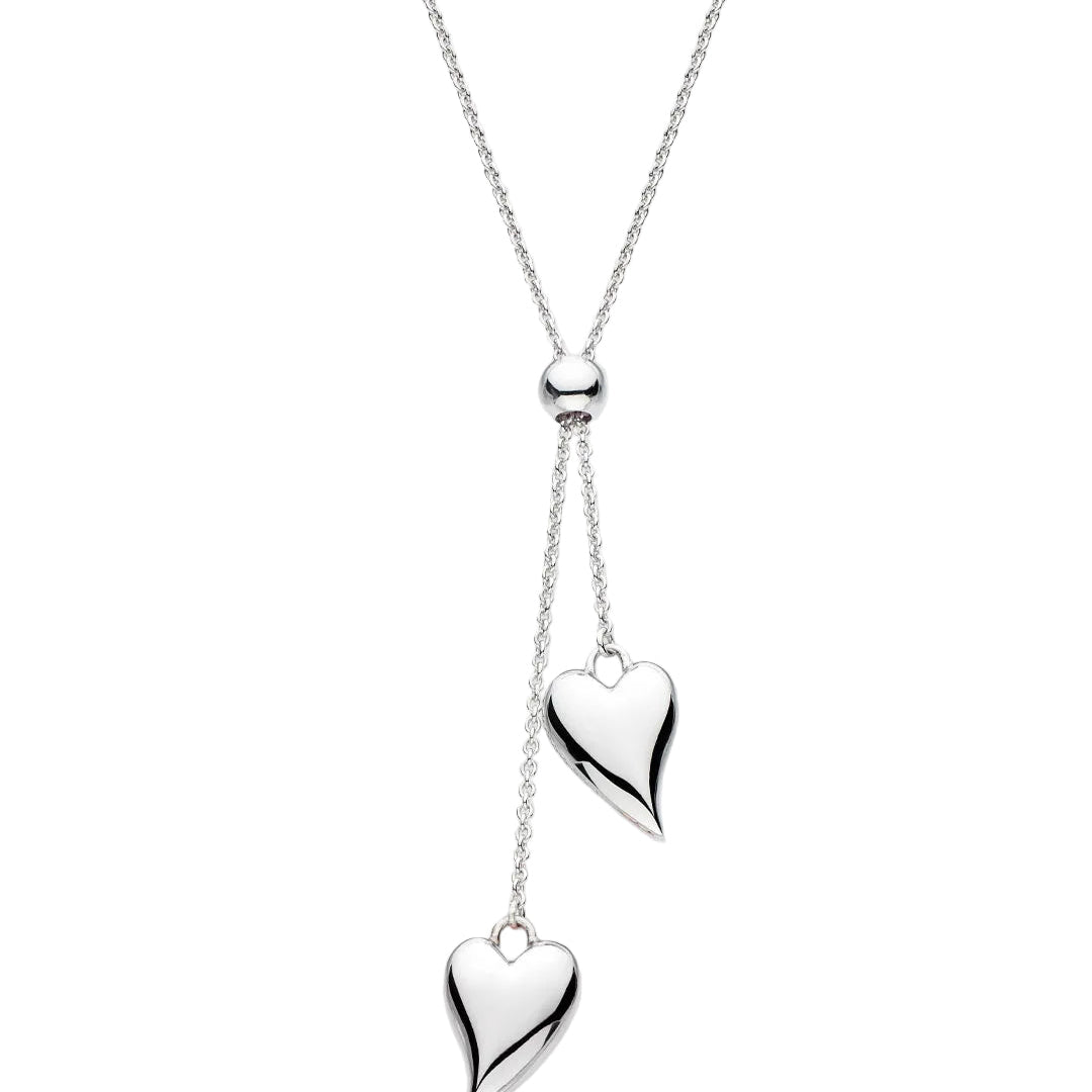 A silver lariat-style necklace with a fine chain, a small polished bead, and two dangling heart charms of different sizes, shown on a light gray background.