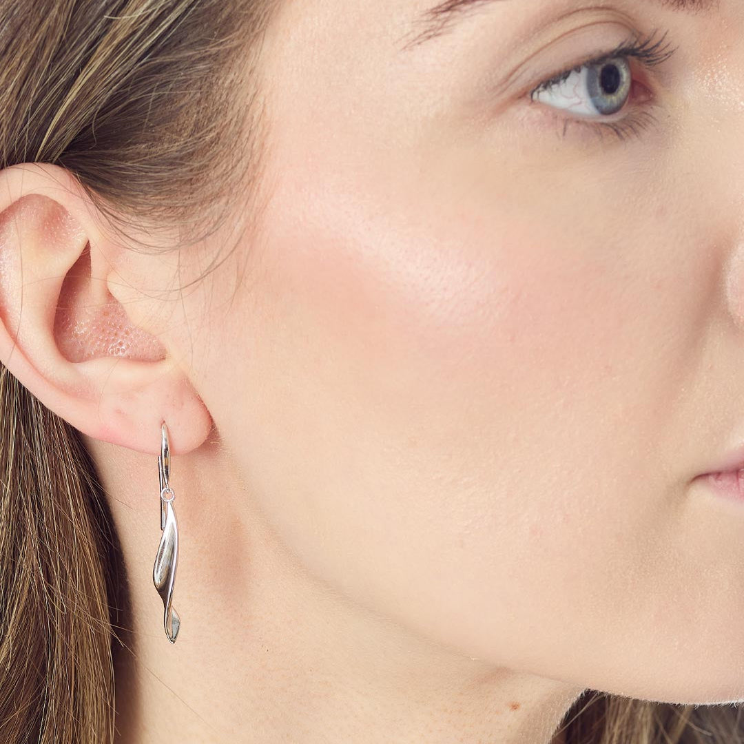 A close-up side profile of a woman wearing a single twisted silver hoop earring.