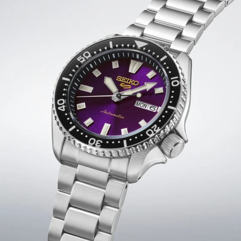 A Seiko dive watch with a silver stainless steel bracelet and case, featuring a prominent purple dial and a black rotating bezel.