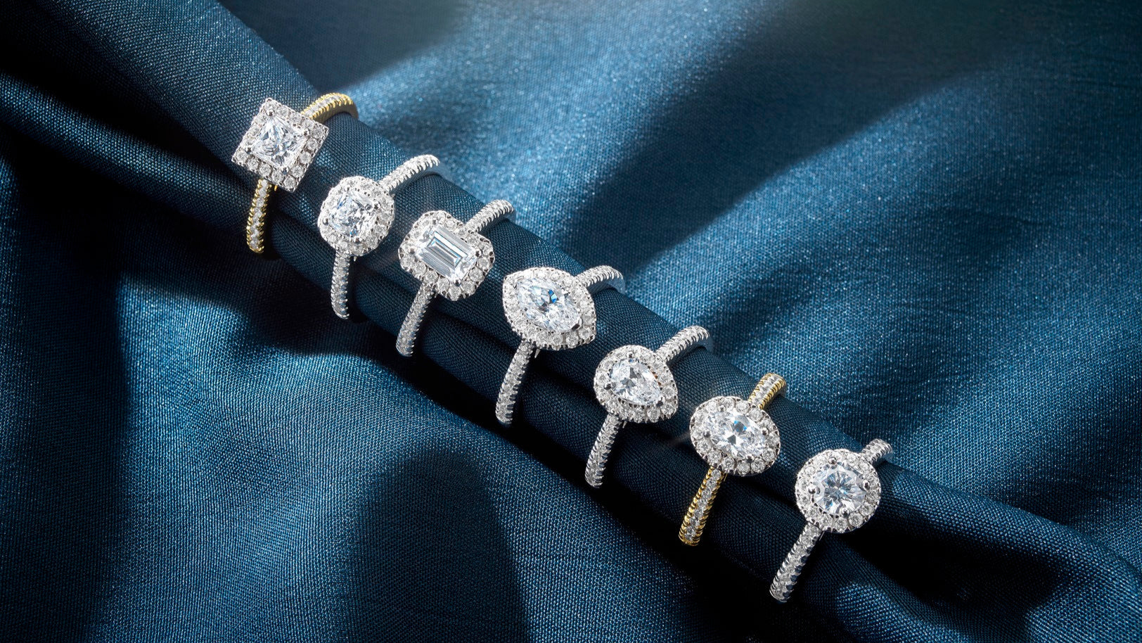 A collection of six diamond engagement rings displayed on elegant dark blue satin fabric